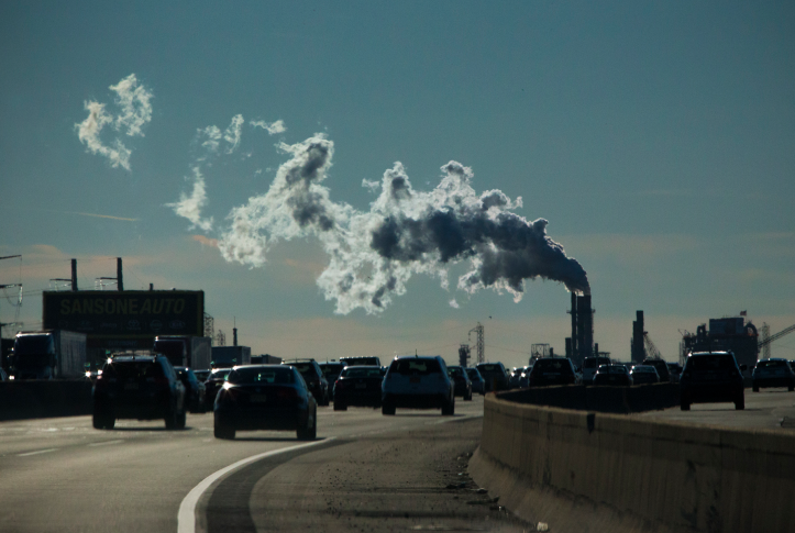 Photo, cars on highway underneath plume of factory smoke