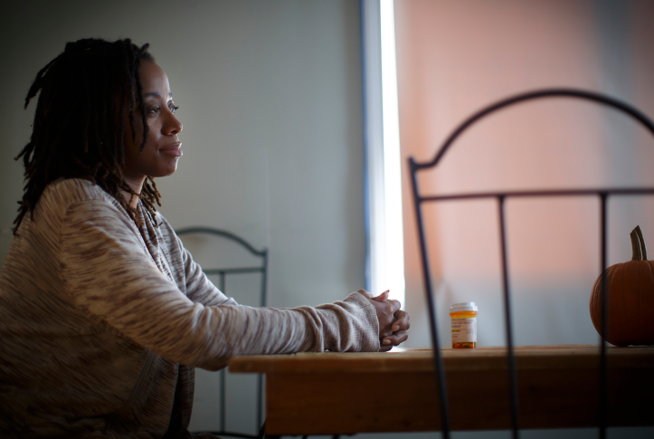 Woman sits at table with prescription drug bottle