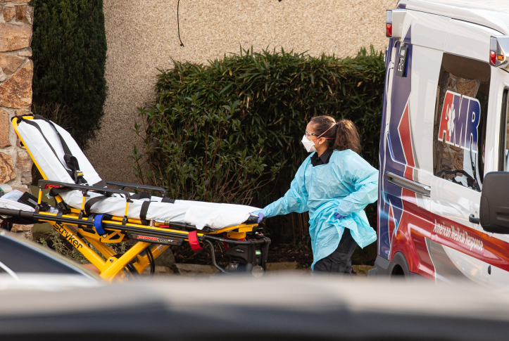 Hospital worker in safety gear loads stretcher out of ambulance