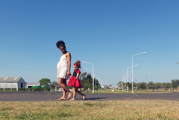 pregnant mom and daughter walk barefoot in front of rural homes