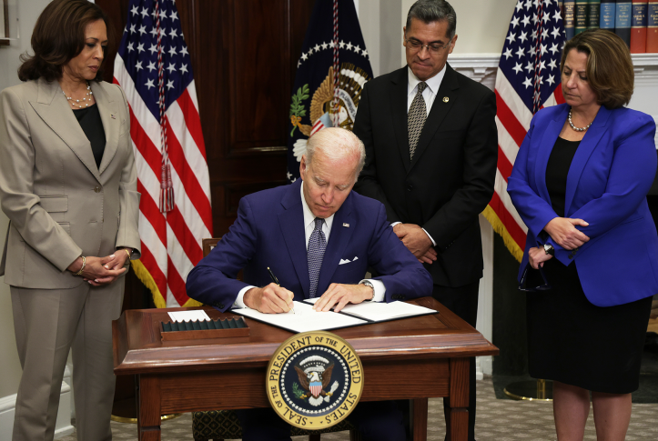 President Biden signing paperwork in front of American flags