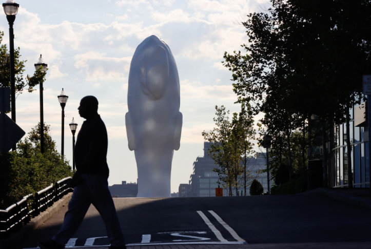 man in silhouette walks across deserted street in front of large sculpture of a head