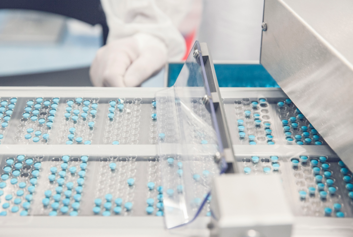 blue pills in machine manufactured with white gloved hand in background