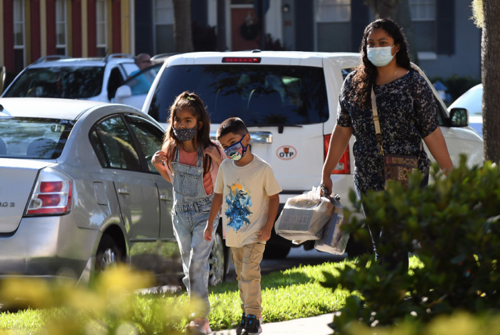 two children in masks walk down street next to parent in mask