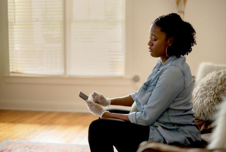 Woman seated scrolling through smartphone wearing gloves