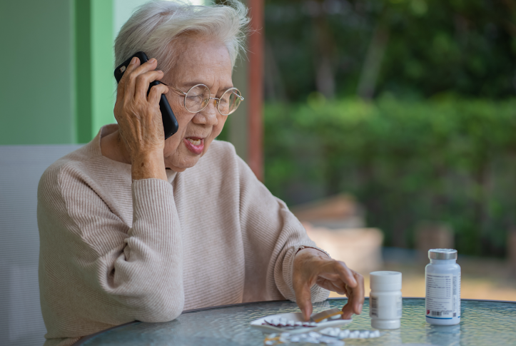 senior woman on phone looks at pill packets on table