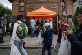 Photo, people walk in front of tent in front of brick building