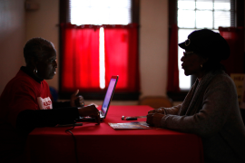 Two people sit on opposite sides of the table while one looks at a laptop