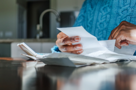 Women's hands hold bills on kitchen counter
