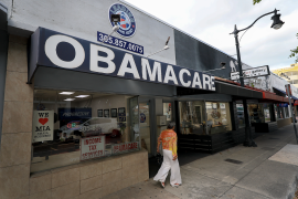 Woman walks in front of storefront that reads Obamacare