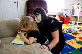 Photo, woman in mask reads to child on couch
