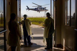 Three medical staff stand in front of open door staring at a helicopter