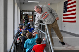 Photo, Man leans over railing to give high five to kids in school