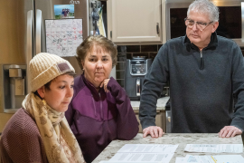 Three people look at bills on counter in kitchen