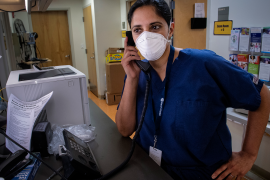 Female physician in scrubs and mask on phone in hospital