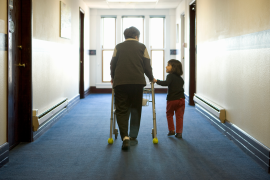 Elderly woman with walker is helped down hallway by young girl