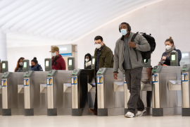 Commuters walk thru terminal in station with masks.