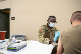 Military doctor gives vaccine to other military member at white table