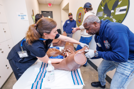 Woman coaching a man through emergency childbirth scenarios with the use of a birthing simulator.