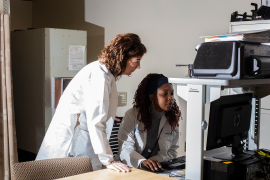 Two lab coat-wearing employees work on computer