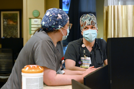 Photo, two nurses talk over desk in masks