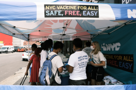 People stand in front of NYC free vaccine sign under a tent