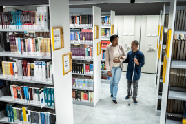 Photo, man with cane walks holding woman's arm in library
