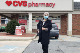 Woman in mask and hat walks outside of CVS pharmacy in parking lot