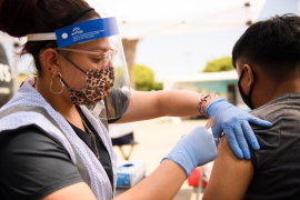 Nurse with mask and face shield gives young teen a COVID vaccine