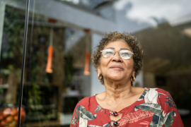 elderly woman in glasses looks up at sky in front of house