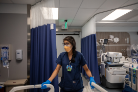 Doctor in mask holds corners of hospital bed