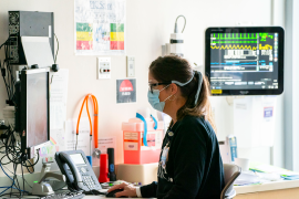 Nurse sits at computer with mask on