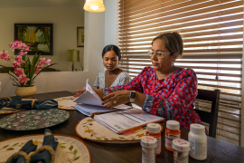 Photo, Woman and daughter sit at table over paperwork with pill bottles in front