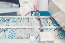 blue pills in machine manufactured with white gloved hand in background