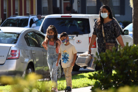 two children in masks walk down street next to parent in mask